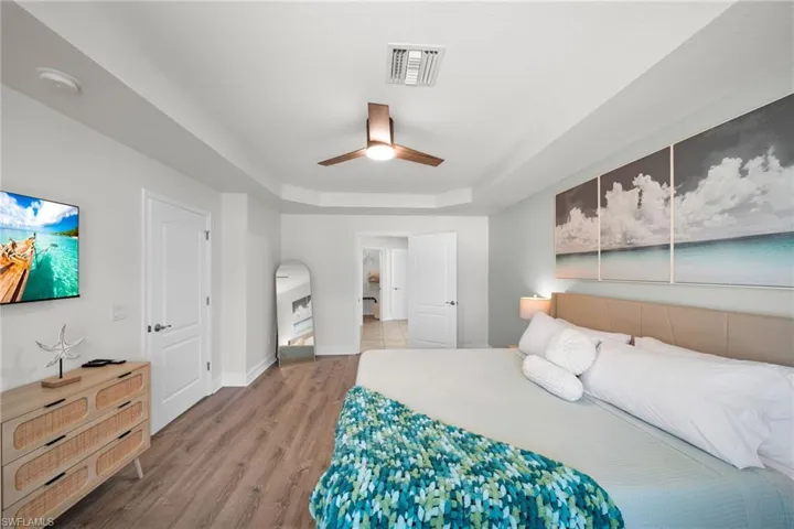 Bedroom featuring ceiling fan, a tray ceiling, visible vents, baseboards, and wood finished floors
