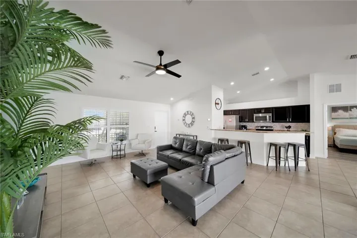 Living area with light tile patterned floors, visible vents, a ceiling fan, and vaulted ceiling