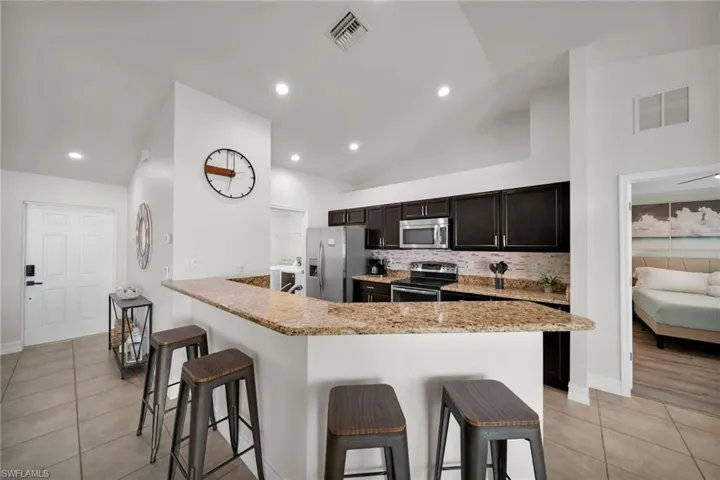 Kitchen featuring vaulted ceiling, visible vents, appliances with stainless steel finishes, and a kitchen bar