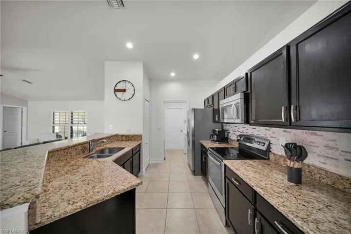 Kitchen with tasteful backsplash, a sink, appliances with stainless steel finishes, light stone countertops, and dark cabinetry