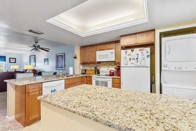 Kitchen with ceiling fan, white appliances, light tile flooring, stacked washer and dryer, and sink