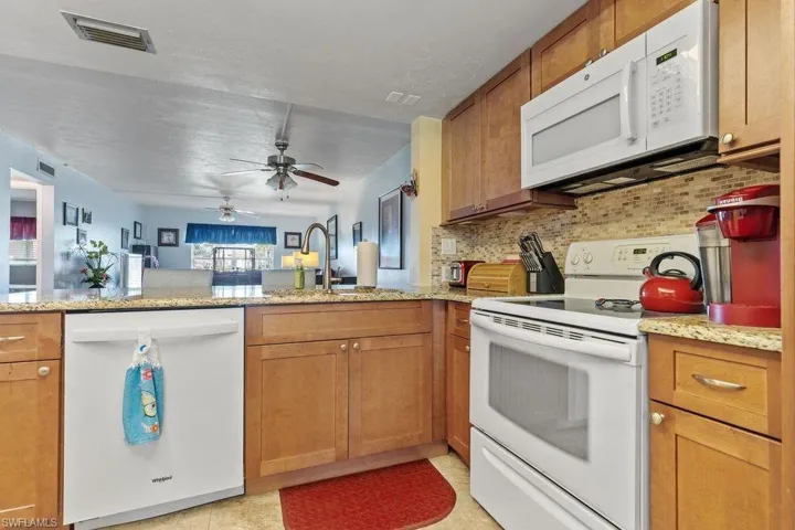 Kitchen featuring light tile flooring, kitchen peninsula, tasteful backsplash, ceiling fan, and white appliances