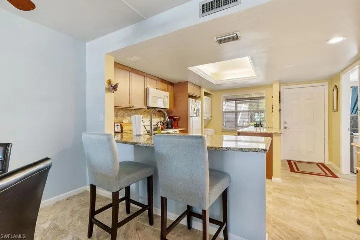 Kitchen featuring light stone countertops, kitchen peninsula, white appliances, and light tile floors