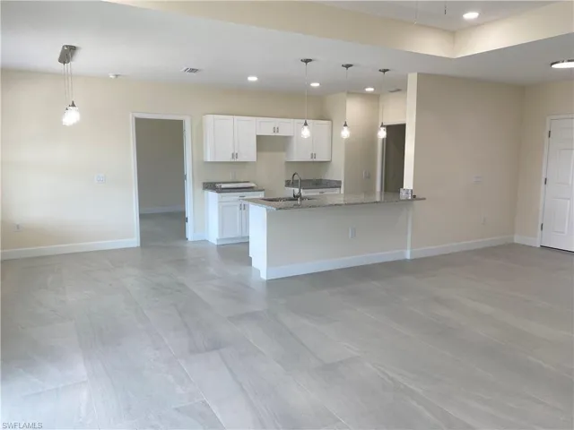 Kitchen with white cabinetry, a peninsula, dark stone countertops, recessed lighting, and decorative light fixtures