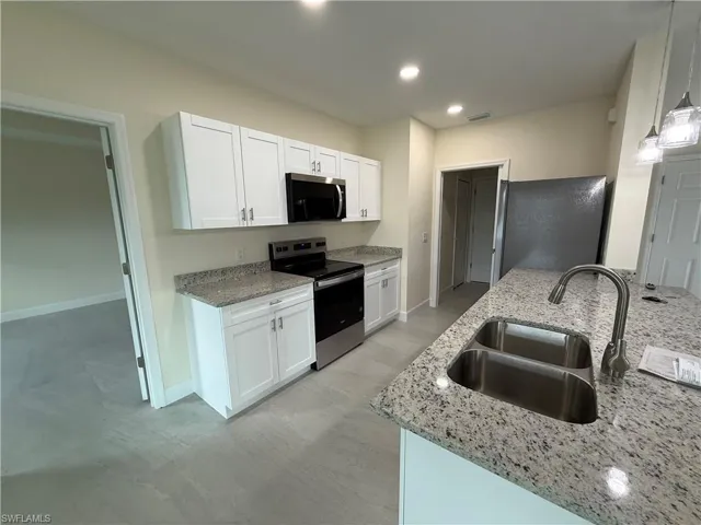 Kitchen featuring appliances with stainless steel finishes, light stone countertops, white cabinetry, and recessed lighting