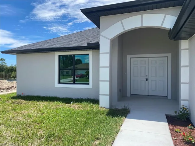Property entrance featuring a lawn, stucco siding, and roof with shingles