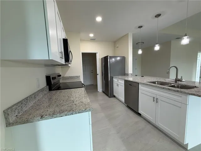 Kitchen featuring light stone countertops, white cabinetry, black appliances, hanging light fixtures, and a peninsula