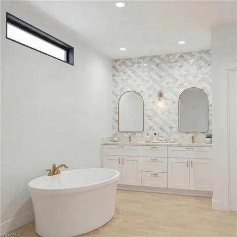 Full bath with a freestanding bath, light wood-style flooring, double vanity, and recessed lighting - Virtually Edited