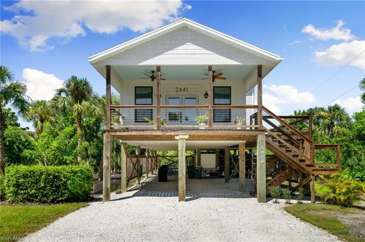Raised beach house with a carport, a ceiling fan, driveway, covered porch, and stairway