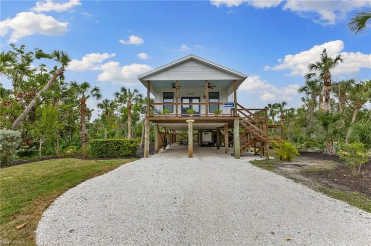 Beach home with ceiling fan, a carport, stairs, driveway, and a wooden deck