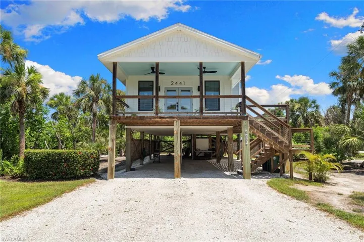 Coastal home with a ceiling fan, a carport, gravel driveway, stairs, and a porch