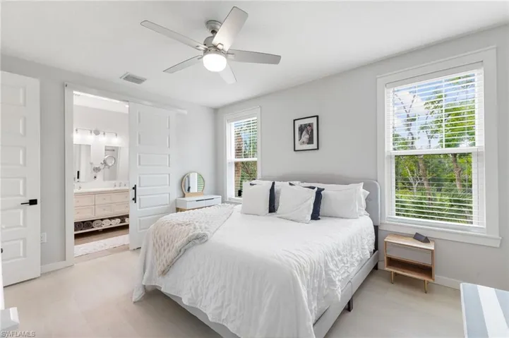 Bedroom with ensuite bathroom, light wood-style flooring, and ceiling fan
