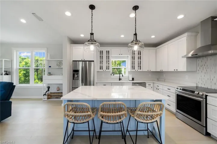 Kitchen featuring stainless steel appliances, wall chimney exhaust hood, a kitchen island, white cabinetry, and light stone counters