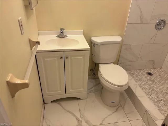 Full bath with marble look tile flooring, a tile shower, toilet, and vanity