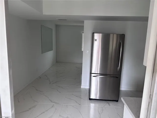 Kitchen with freestanding refrigerator, light marble finish floors, and baseboards