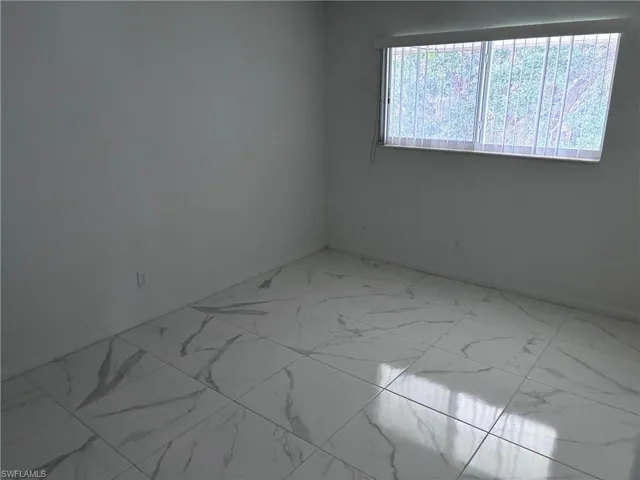 Empty room featuring marble look tiles and baseboards