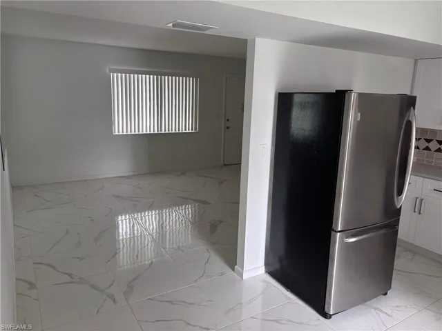 Kitchen with freestanding refrigerator, light marble finish floors, white cabinets, and baseboards