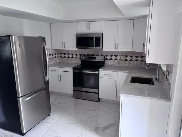 Kitchen with stainless steel appliances, a sink, light marble finish flooring, and white cabinets