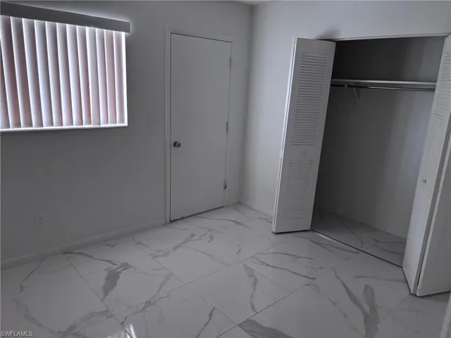 Unfurnished bedroom featuring marble finish flooring, a closet, and baseboards