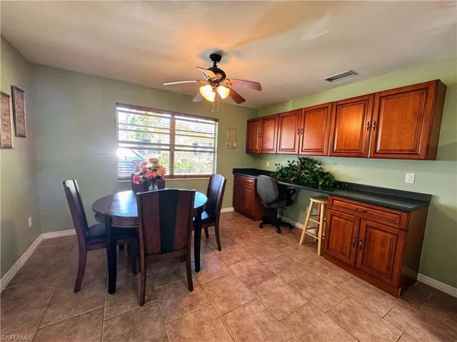 Dining room with ceiling fan, light tile patterned flooring, visible vents, baseboards, and built in study area