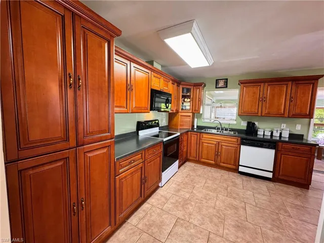 Kitchen with black microwave, range with electric stovetop, a sink, dishwasher, and dark countertops