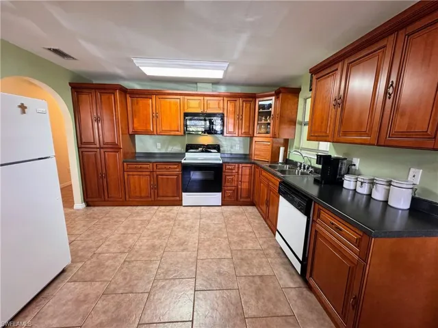 Kitchen featuring white appliances, a sink, visible vents, brown cabinetry, and dark countertops