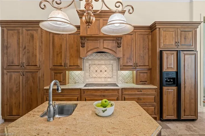 Well-appointed chef’s kitchen featuring custom wood cabinetry, granite countertops, a center island, stainless steel appliances, and an elegant decorative range hood.