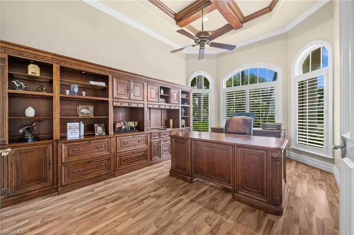Private study featuring extensive custom built-ins, rich wood flooring, and elegant arched windows that fill the space with natural light.