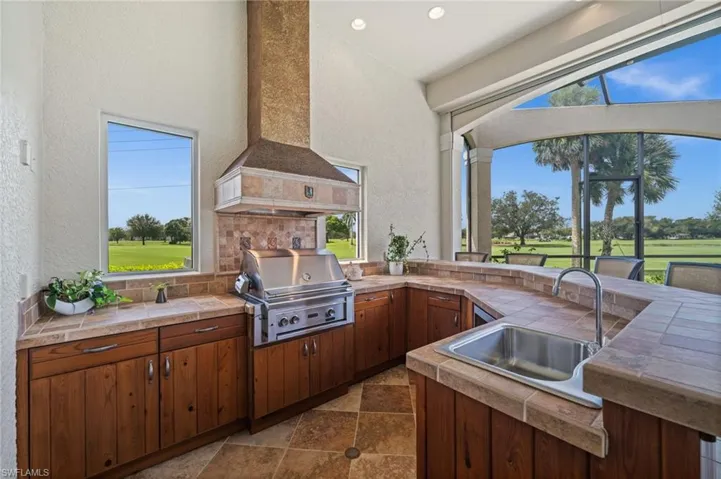 Built-in summer kitchen featuring abundant cabinetry, a grill, and picturesque views of the pool and golf course beyond.