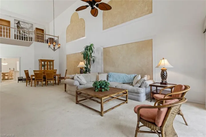 Living area featuring a towering ceiling, ceiling fan, light colored carpet, and a chandelier