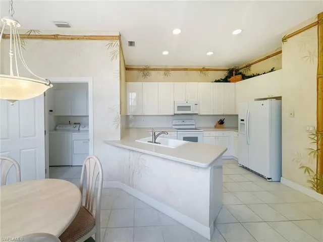 Kitchen with white appliances, washing machine and clothes dryer, white cabinets, light countertops, and recessed lighting