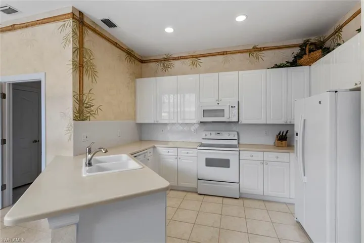 Kitchen with white appliances, a sink, a peninsula, wallpapered walls, and light countertops
