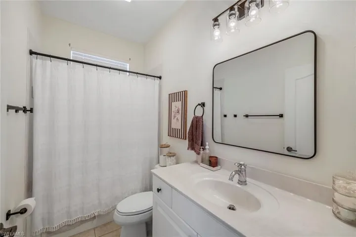 Bathroom featuring a white vanity with a single basin, a rectangular mirror with a black frame, and a shower with a white curtain