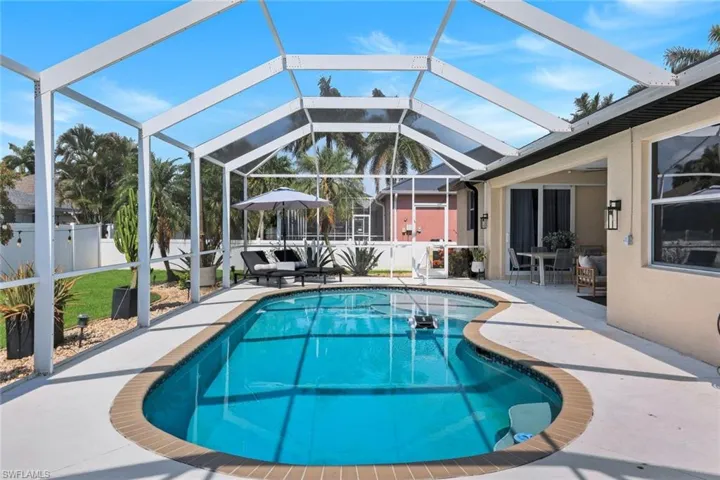 Screened outdoor living area featuring a freeform swimming pool with brick coping, a spacious pool deck, and exterior wall sconces