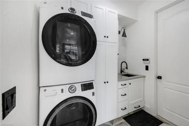 Dedicated laundry area featuring stacked appliances, white shaker cabinetry, a utility sink with a matte black faucet, subway tile backsplash, and a light gray countertop