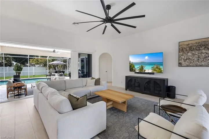 Spacious living area featuring light-toned flooring, a large black ceiling fan, and an arched doorway