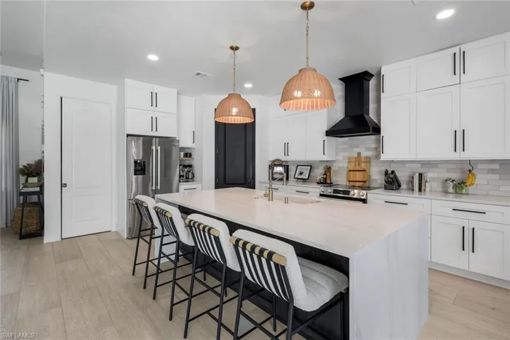 Spacious kitchen featuring a large central island with seating, white shaker cabinetry, stainless steel appliances, and wood-finish flooring