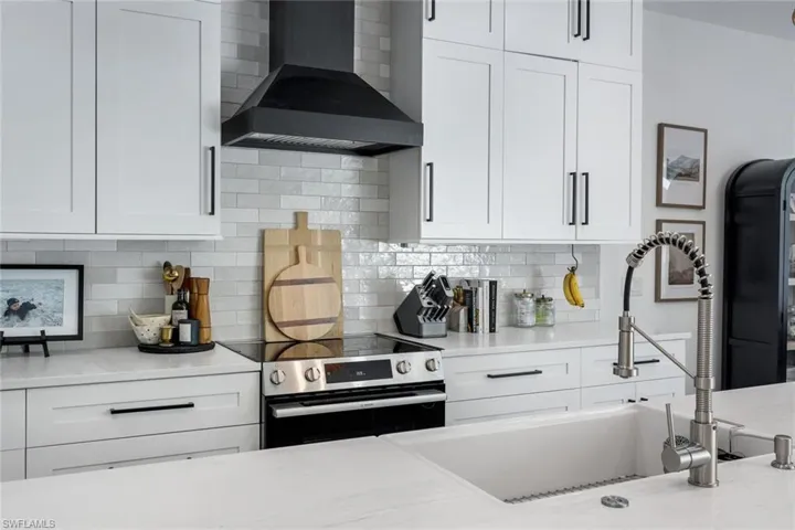 Modern kitchen featuring white shaker cabinetry with matte black hardware, a white subway tile backsplash, and a black range hood