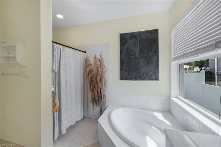 Built-in soaking tub with white tile surround, privacy window with blinds, recessed lighting, and hexagonal floor tiling