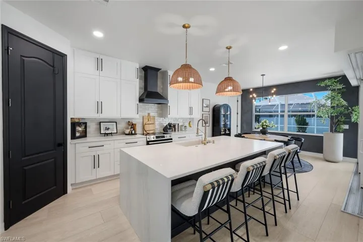 Kitchen featuring a large central island with seating, pendant lighting, white cabinetry, and light-tone wood-finish flooring