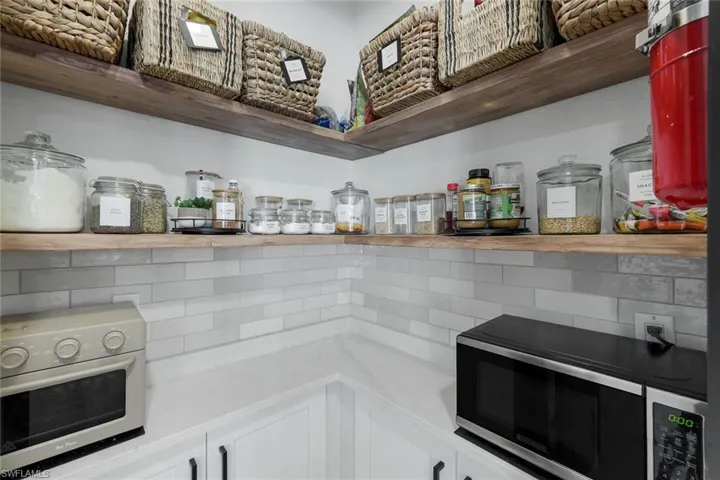 Pantry featuring white subway tile backsplash, white cabinetry with black hardware, and wood-finish open shelving
