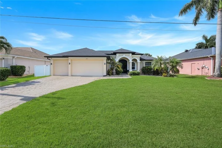 Cream-colored stucco exterior with a dark shingle roof, featuring an arched entry, a two-car garage, and a paver driveway