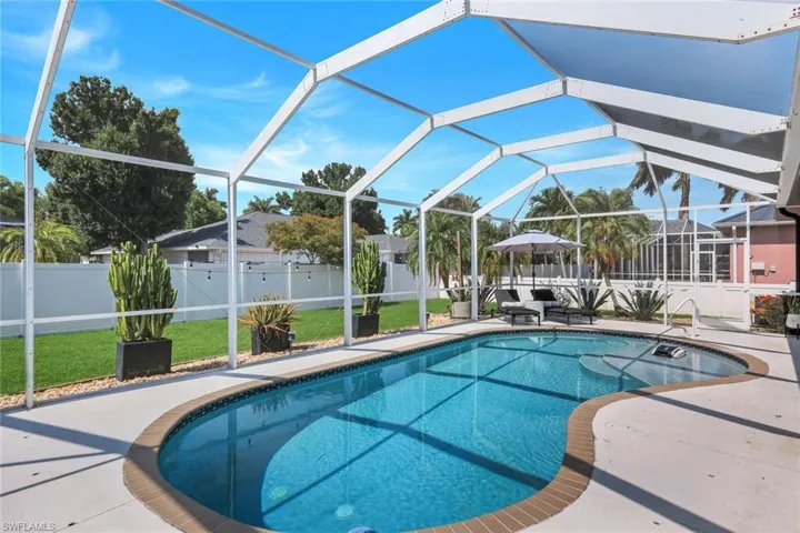 Screened outdoor pool area featuring a freeform pool with a textured tile border, a spacious concrete paver deck, and a white privacy fence