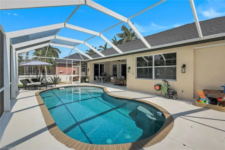 Screened-in outdoor living space featuring a freeform swimming pool with a brick coping, an expansive paved patio, and a covered lanai
