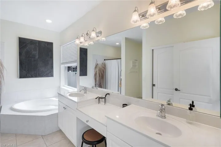 Bathroom featuring a built-in corner soaking tub, dual vanity with undermount sinks, and a full-width wall mirror