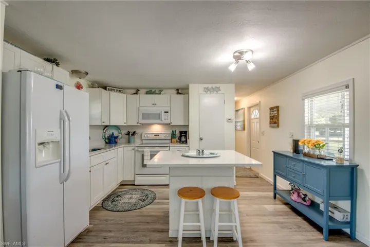 Kitchen featuring white appliances, a kitchen breakfast bar, white cabinetry, light wood-type flooring, and a kitchen island
