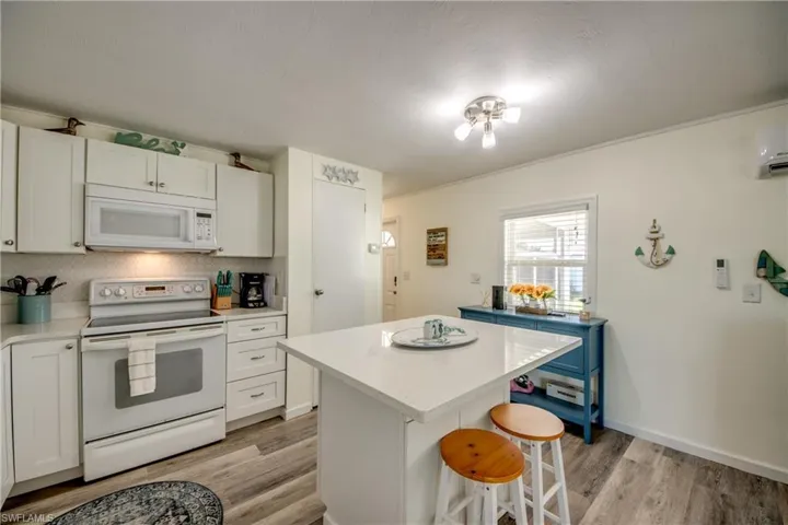 Kitchen featuring white appliances, white cabinets, a breakfast bar, light wood-style floors, and decorative backsplash