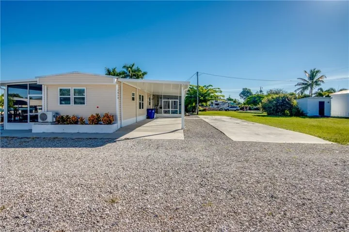 Manufactured / mobile home featuring gravel driveway, a carport, a front yard, and a sunroom