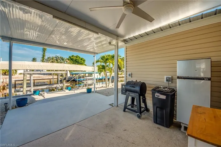 View of patio featuring boat lift, a dock, a water view, a grill, and ceiling fan