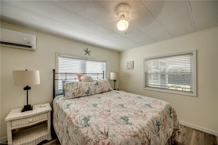 Bedroom with wood finished floors, an AC wall unit, ceiling fan, and a textured ceiling
